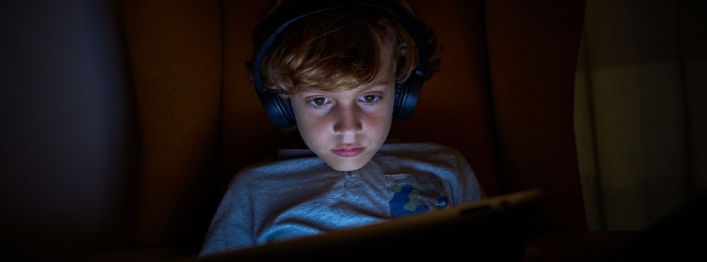 Enfant dans le noir qui semble hypnotisé par la tablette.