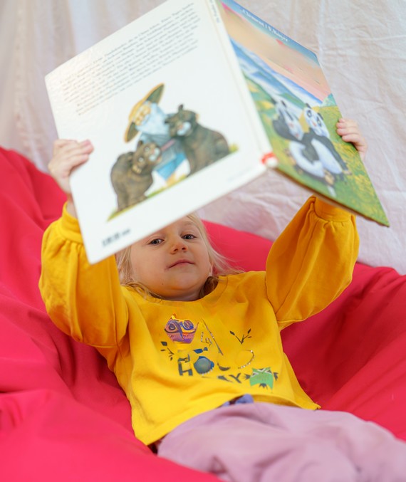 une petite fille assise dans un pouf tient un livre aussi grand qu'elle