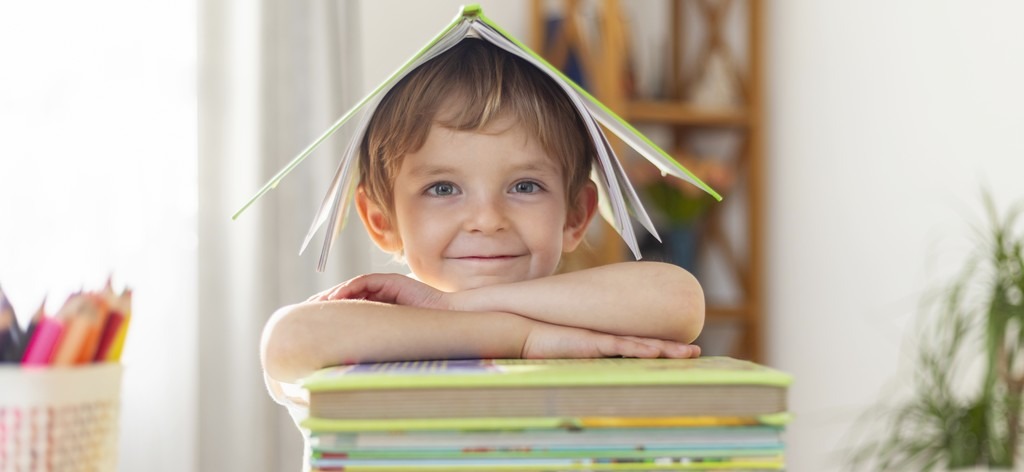 un enfant heureux posé sur une pile de livre et il porte un livre comme chapeau