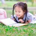 une jeune fille avec des couettes lit un livre dehors avec ses peluches