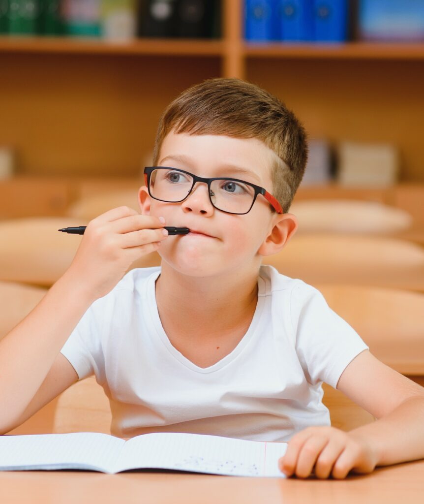 un enfant avec des lunettes qui réfléchit au dessus d'un livre