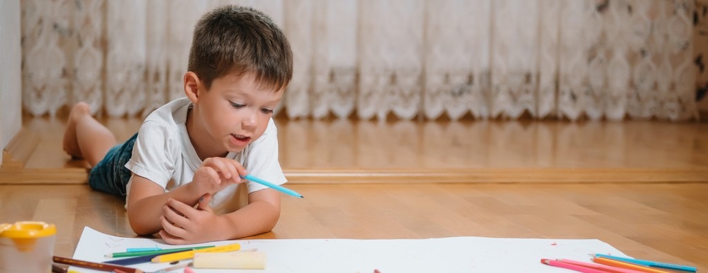 un enfant sur le sol entouré de crayons et feutres, dessine