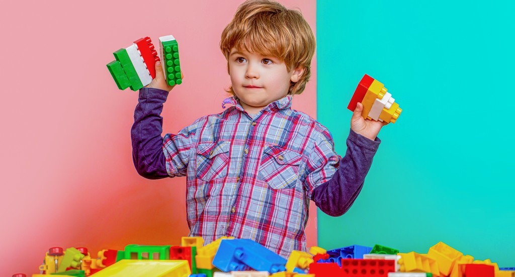 un jeune enfant montre ses jouet de construction sur un fond coloré