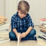 un garçon qui semble réticent à ouvrir un livre entouré de piles de livres