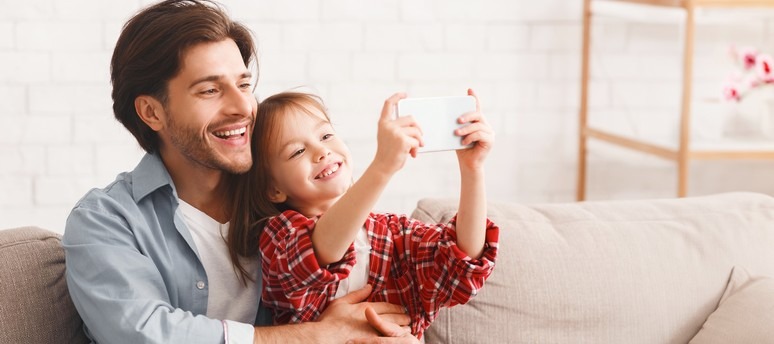 Un père et sa fille sur le canapé en train de jouer sur un smartphone