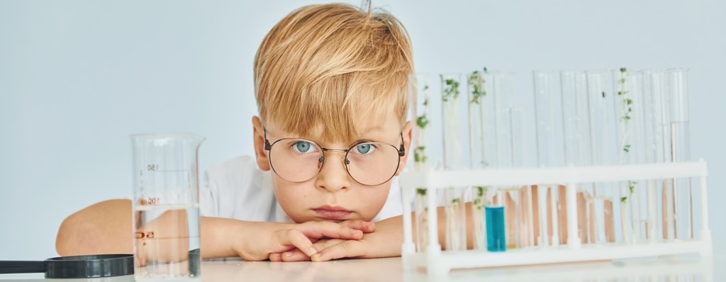 un enfant avec des lunettes, calme avec une loupe, un bécher et des tubes à essai. 