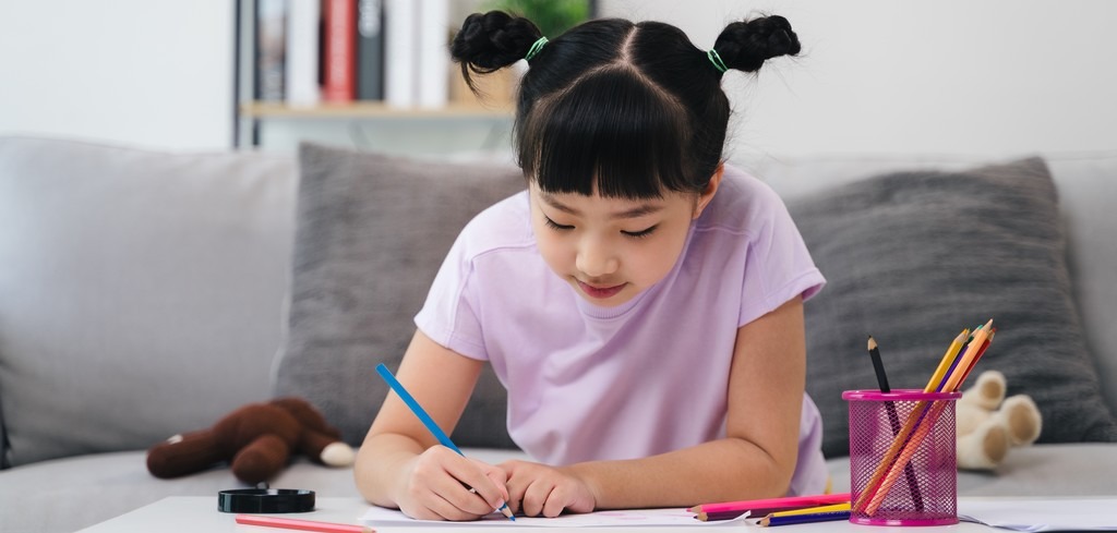 une jeune fille, assise sur un canapé dessine avec des crayons