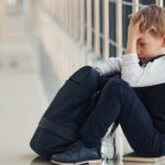 un garçon assis sur le sol, triste, se tient la tête