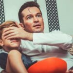 un père et son fils devant la télé, le pere cache les yeux de l'enfant pour qu'il ne vois pas le contenu horrifique