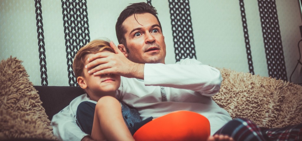 un père et son fils devant la télé, le pere cache les yeux de l'enfant pour qu'il ne vois pas le contenu horrifique