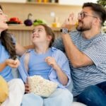 une famille sur un canapé qui s'apprête à regarder la télé avec un bol de popcorn