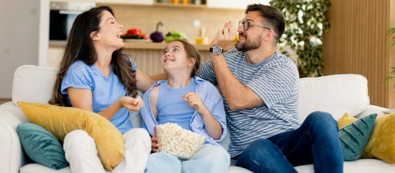 une famille sur un canapé qui s'apprête à regarder la télé avec un bol de popcorn