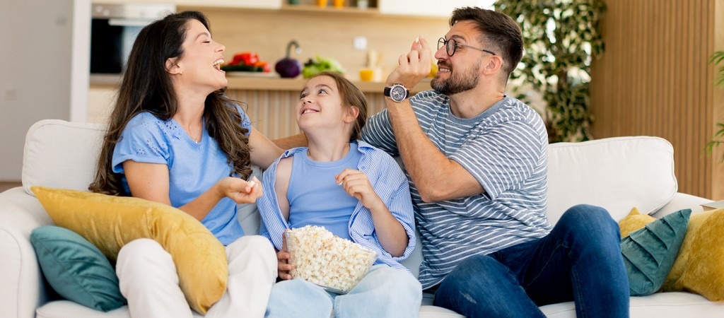 une famille sur un canapé qui s'apprête à regarder la télé avec un bol de popcorn