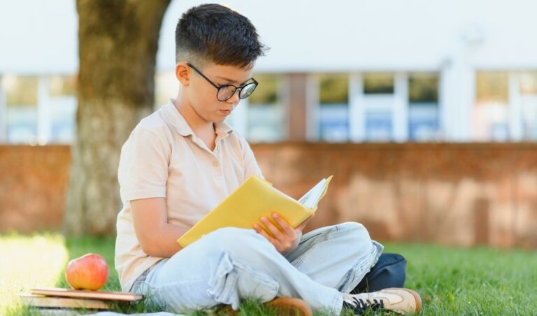 un enfant lit et révise dehors dans l'herbe