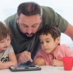 un parent regarde attentivement le contenu de la tablette avec ses enfants