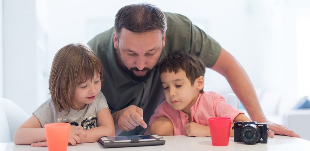 un parent regarde attentivement le contenu de la tablette avec ses enfants