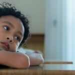un enfant, la tête posée sur son bureau, il s'ennuie